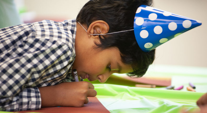 Boy wearing a birthday hat coloring with a crayola crayon